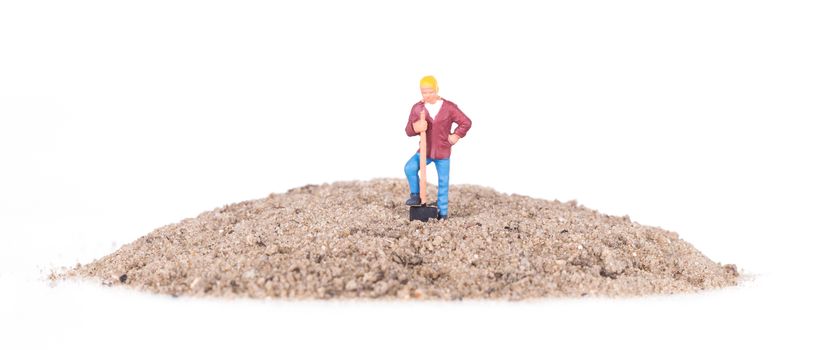 Miniature worker with a shovel on a mountain of sand