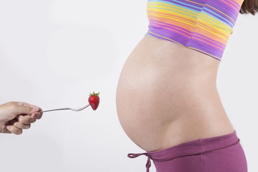 offering strawberry to tummy of naked pregnant woman
