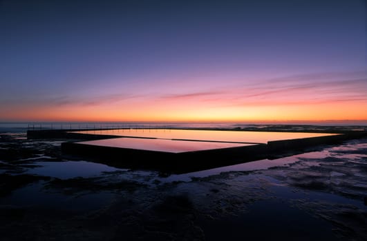 Beautiful colours in the sky about hour before sunrise at Wambarra, NSW, Australia and vivid reflections in the rock pool.
