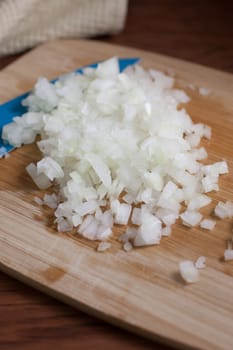 Fresh chopped onions and a blue ceramic knife on a wooden cutting board.