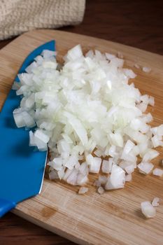 Fresh chopped onions and a blue ceramic knife on a wooden cutting board.