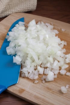 Fresh chopped onions and a blue ceramic knife on a wooden cutting board.