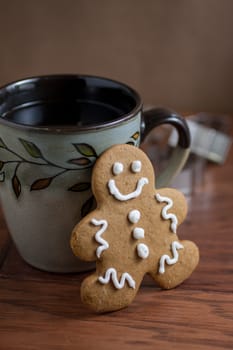 A gingerbread man cookie and a cup of fresh coffee on a wooden table.