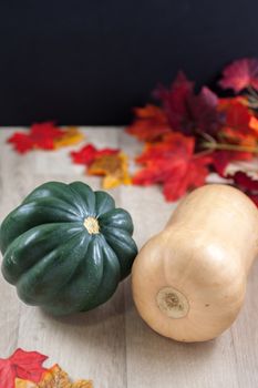 Acorn and Butternut squash on a table with fall leaves in the background.
