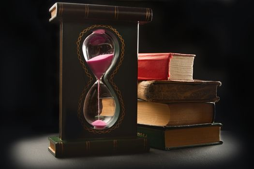 Pile of old books and sand glass on black