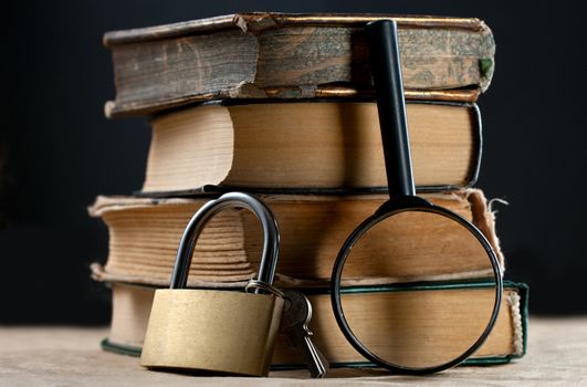 Pile of old books with keylock and magnifying glass