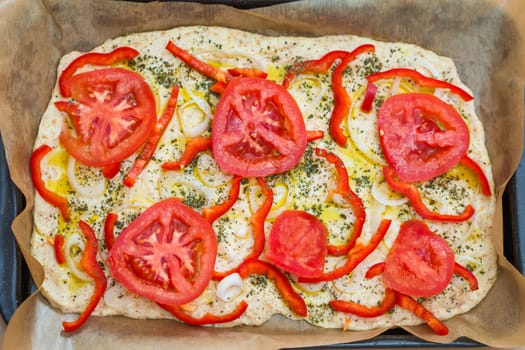 Delicious fresh traditional Italian focaccia bread with tomatoes, red peppers, onions, basil and olive oil on pan ready to cook