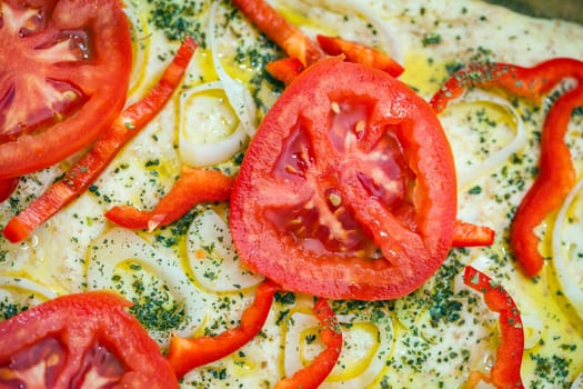 Tomato slice detail of traditional Italian focaccia bread with red peppers, onions, basil and olive oil on pan ready to cook