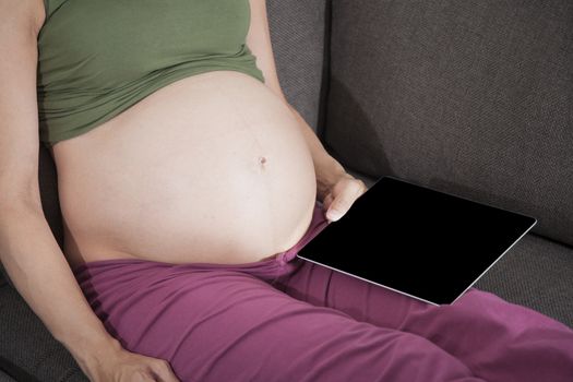 pregnant woman reading tablet sitting in sofa