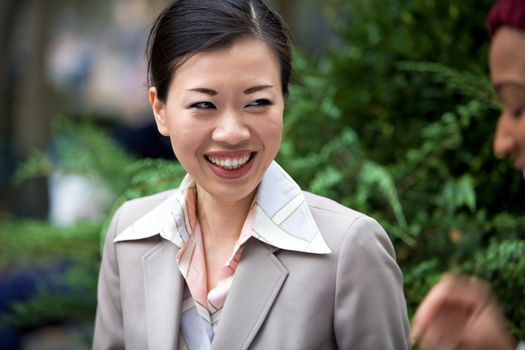 An attractive Asian woman dressed in business attire laughing at the words of her business associate.