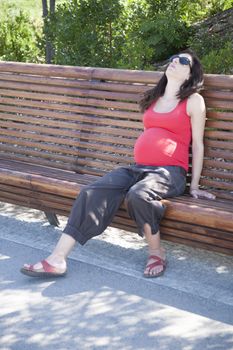 pregnant woman tired sitting on a bench resting