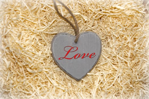 single grey wooden love heart in a love nest made of straw inscribed in red