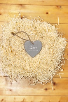 single grey wooden love heart in a love nest made of straw inscribed love is a sweet thing on floor boards