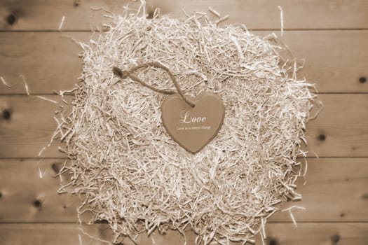 single sepia wooden love heart in a love nest made of straw inscribed love is a sweet thing on floor boards