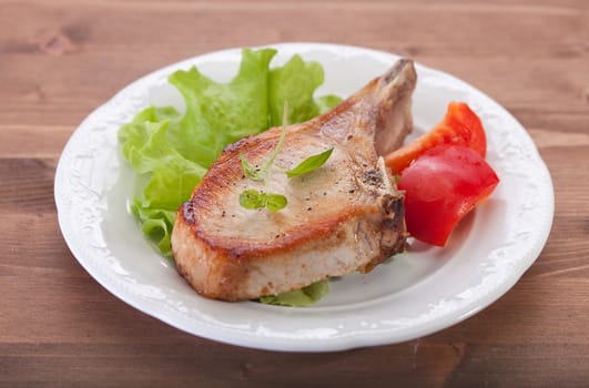 White plate with fried pork cutlet, lettuce and red sweet pepper on the wooden table