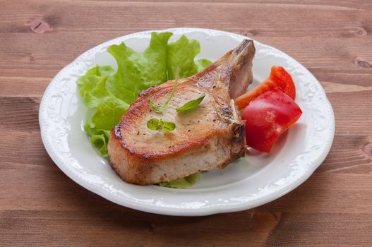 White plate with fried pork cutlet, lettuce and red sweet pepper on the wooden table