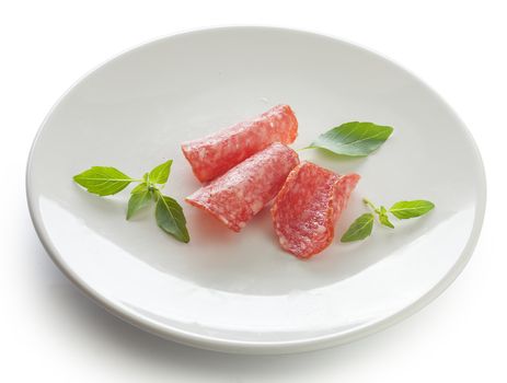 Three pieces of smoked sausage with fresh green basil on the white plate