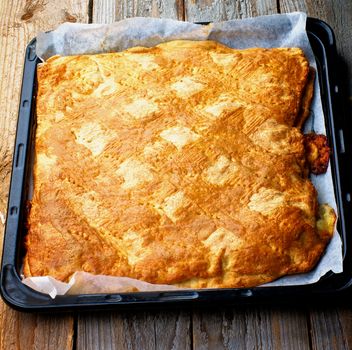 Homemade Closed Cheese Pie on Black Oven with Parchment Paper closeup on Rustic Wooden background
