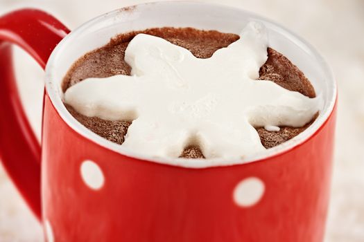 Vibrant red cup of hot chocolate with snow flake shape of whipped cream. Extreme shallow depth of field.