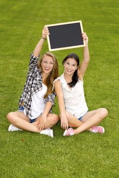 Tennage students sitting on the grass and holding a chalkboard