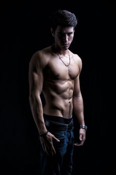 Handsome shirtless muscular young man's profile, looking at camera, on dark background