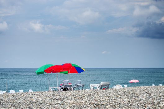 Sun umbrellas stuck in a pebble beach with blue sea