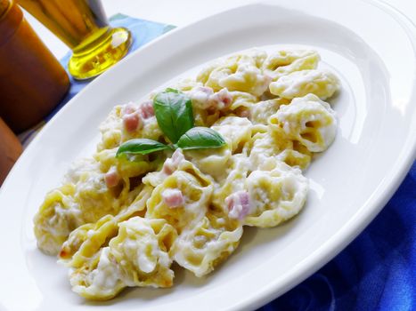 Italian food close-up view of a fresh and genuine pasta tortellini with cream, ham and basil for mediterranean menu and restaurant background.