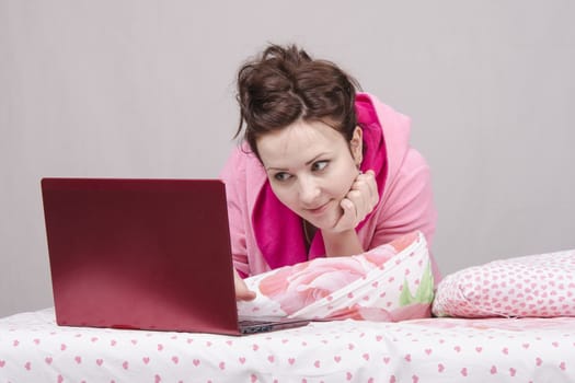 The girl lying in bed and works in the laptop