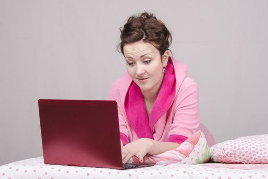 The girl lying in bed and works in the laptop