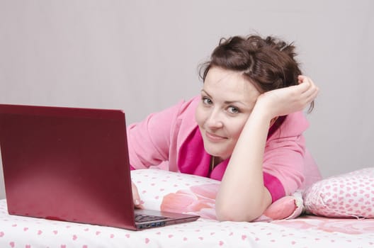 The girl lying in bed and works in the laptop