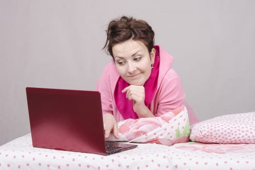 The girl lying in bed and works in the laptop