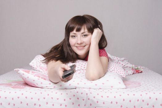The girl lying in bed and watching TV