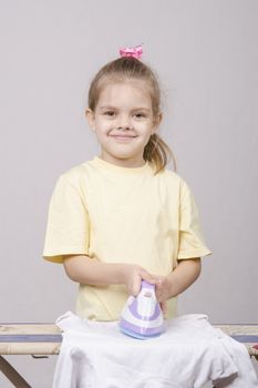 A five year old girl playing in a housewife, and stroking things iron