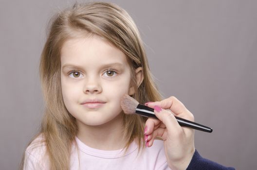 Makeup artist deals powder brush on the face of a five year old girl
