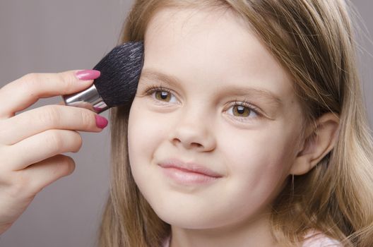 Makeup artist deals powder brush on the face of a five year old girl
