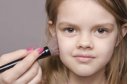 Makeup artist deals powder brush on the face of a five year old girl