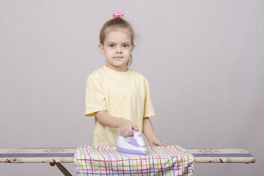 A five year old girl playing in a housewife, and stroking things iron