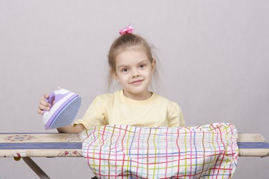 A five year old girl playing in a housewife, and stroking things iron