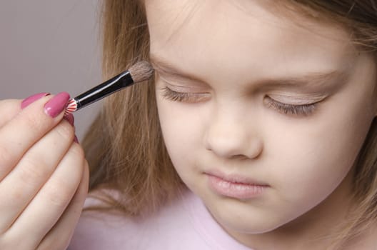 Makeup artist in the process of makeup colors eyelids on the face five year old girl
