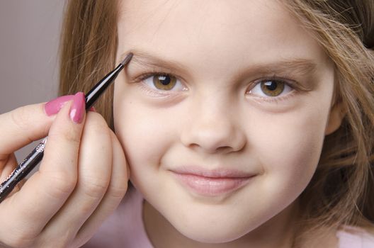 Makeup artist in the process of makeup brings eyebrows on the face five year old girl