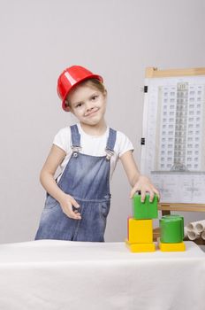 Girl playing in the Builder builds a set of cubes house. In the background on the easel fixed drawing of a house