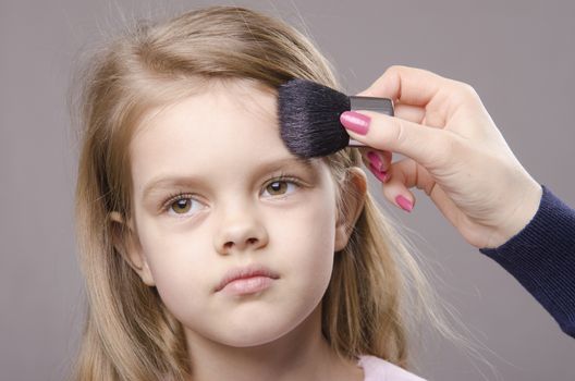 Makeup artist deals powder brush on the face of a five year old girl