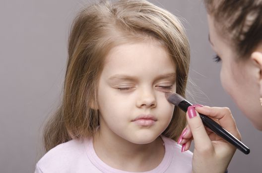 Makeup artist deals powder brush on the face of a five year old girl