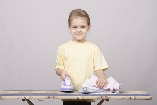 A five year old girl playing in a housewife, and stroking things iron