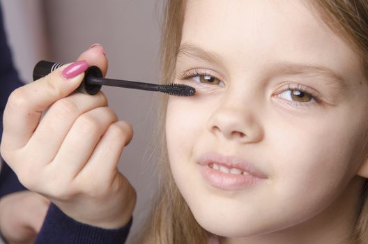Makeup artist in the process of makeup colors eyelashes on the face five year old girl