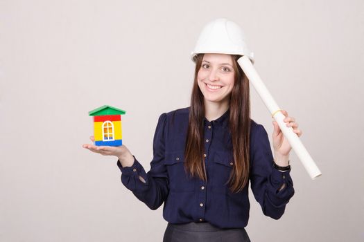 Young woman builder in helmet and with a house worth drawing in the hands of