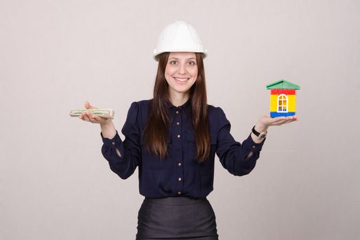 Young woman builder in helmet with little house and worth the money in the hands of