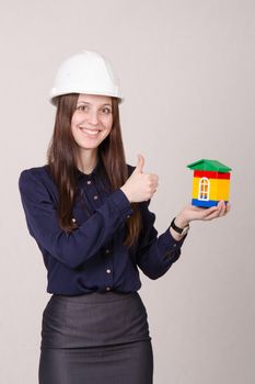 Young woman builder in helmet with a house worth in the hands of