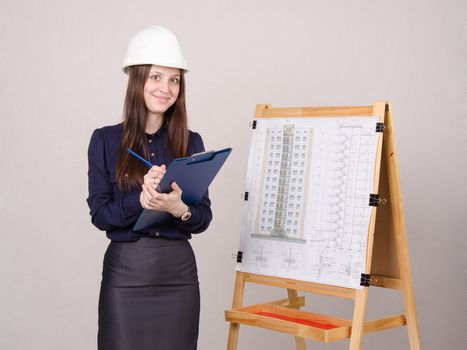 Young woman architect standing at drawing board mounted on the project of a multistory building