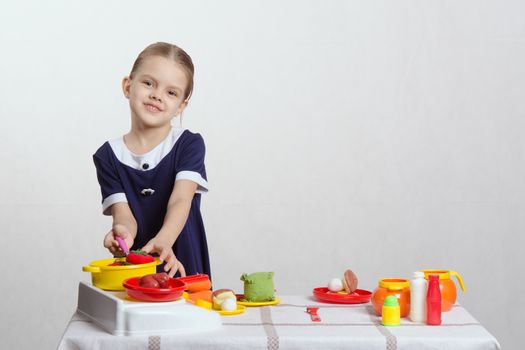 Five year old girl playing in a children's mistress dishes at a table covered with a cloth